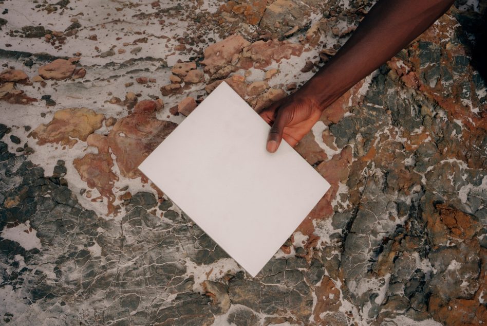 Hand holding blank white card for mockup design on textured multicolored stone surface, ideal for graphics display.